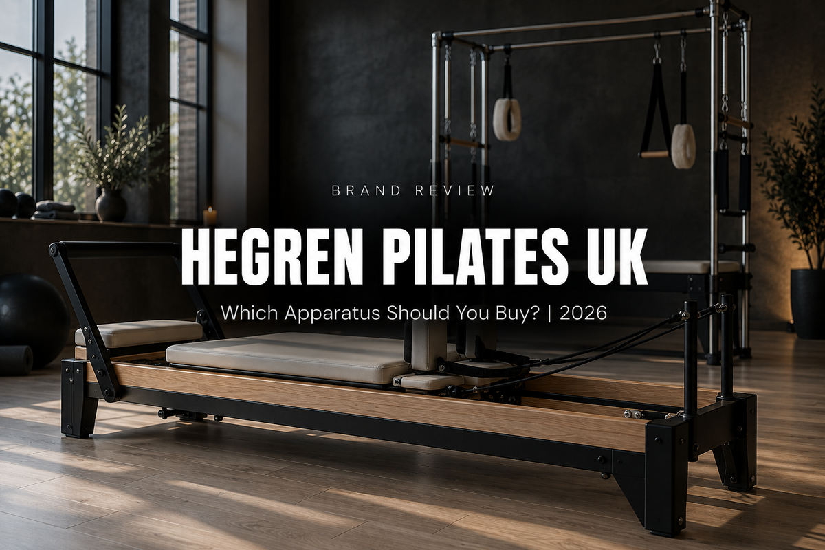 A professional Pilates reformer with a black steel frame and cream upholstery in a premium studio with a Cadillac trapeze behind it