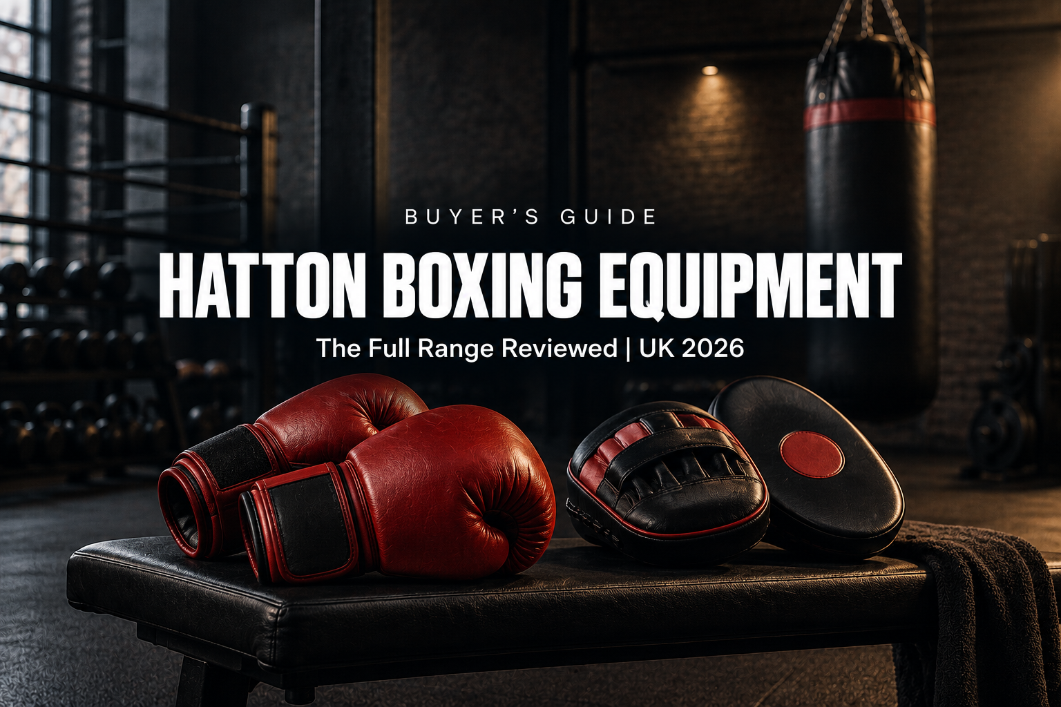 Red leather boxing gloves and focus pads on a bench with a heavy punch bag in the background in a dark UK gym