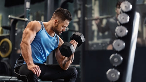 Man in blue vest lifting a dumbbell with gym equipment in the background